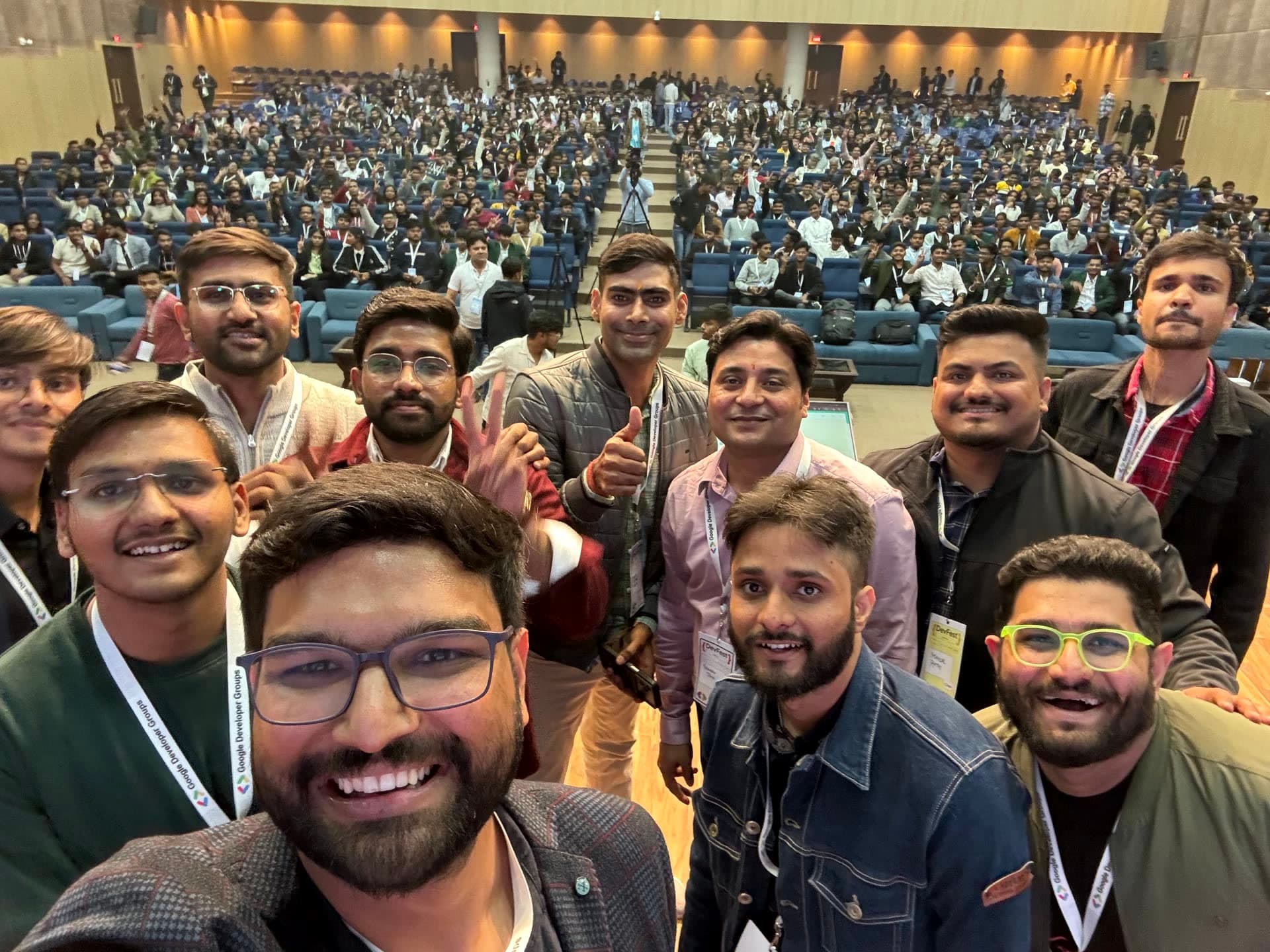 Stage selfie by organizers and leads with the entire packed hall waving hands at DevFest Bhopal 2024